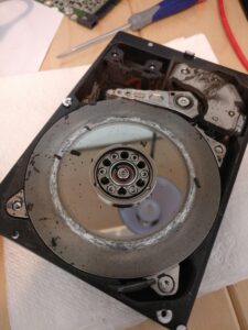 Opened hard drive showing the platter and read-write arm that cause a clicking noise when the drive fails
